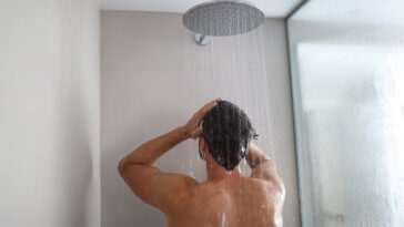Man taking a shower washing hair under water falling from rain