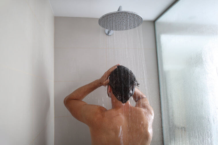 Man taking a shower washing hair under water falling from rain