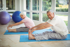 Senior couple performing stretching exercise on exercise mat at